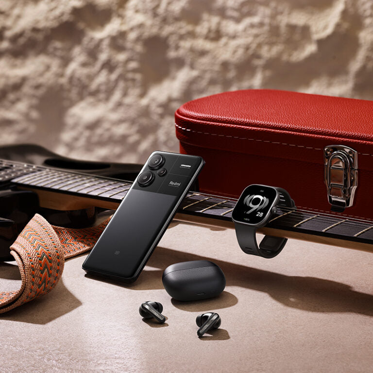 Redmi Watch with fitness tracking displayed on guitar with matching black smartphone and earbuds by GADGETGYZ